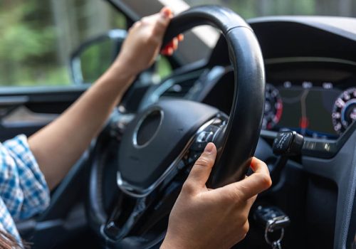 Close-up of female hands on the steering wheel of a modern car while driving. Dashboard and interior details visible. Atmosphere of safety, modernity and style.